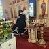 Fr. Aleksey, wearing a black vestment, stands facing the open Royal Doors as he uplifts a white cloth towards the heavens. The tomb and flowers appear behind him, in the lower-left corner.