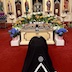 Fr. Aleksey is kneeling and bowing before the Epitaphios, which is surronded by the tomb and flowers. The iconstasis appears in the background.
