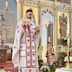 Fr. Aleksey is standing in front of the open Royal Doors, facing the congregation, while reading from a prayer sheet in his left hand. He's wearing white vestments with red ornamentation and is holding a bouquet of candles in his right hand.