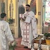 Fr. Aleksey is facing left, holding the Royal Gifts, with his back facing the open Royal Doors. There's an altar server standing in front of him and facing him.