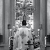 Black and white photo of Fr. Aleksey standing before the Royal Doors with his back facing the congregation.
